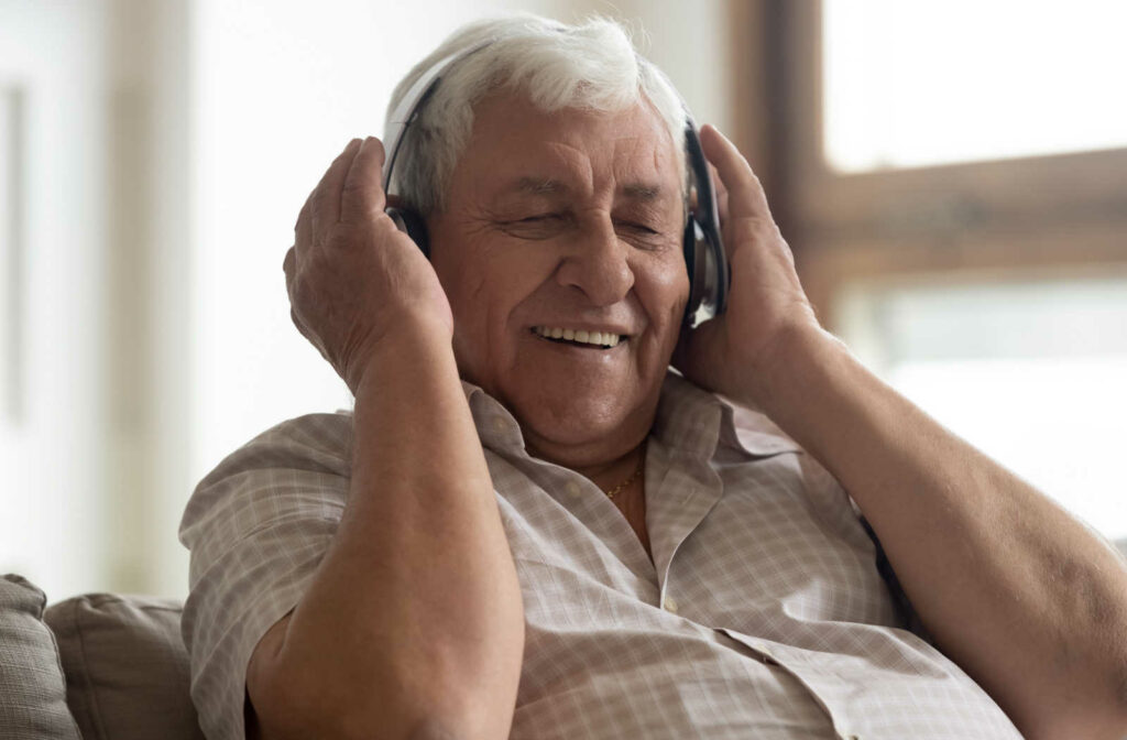 A senior man sitting on a couch wearing headphones and listening to music.