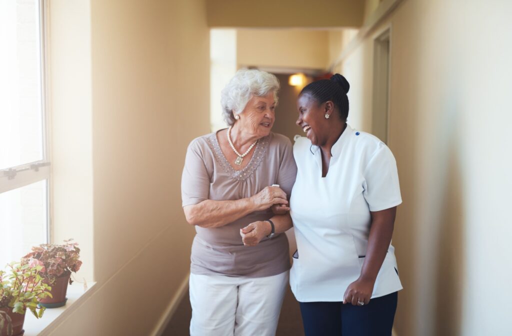 A senior woman walking hand in hand and smiling with a female caregiver.