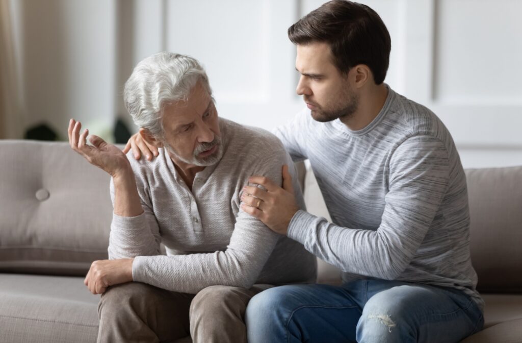 An adult child listening to their parent and comforting them on the couch while discussing a move to memory care.