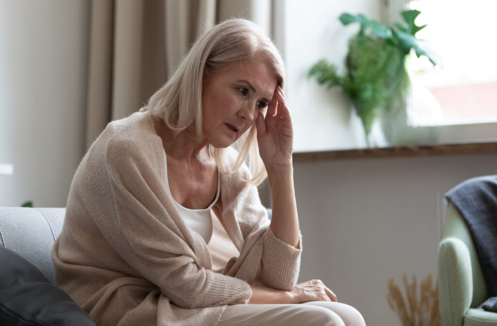 An older adult sitting on their couch, rubbing their forehead in frustration due to memory loss.