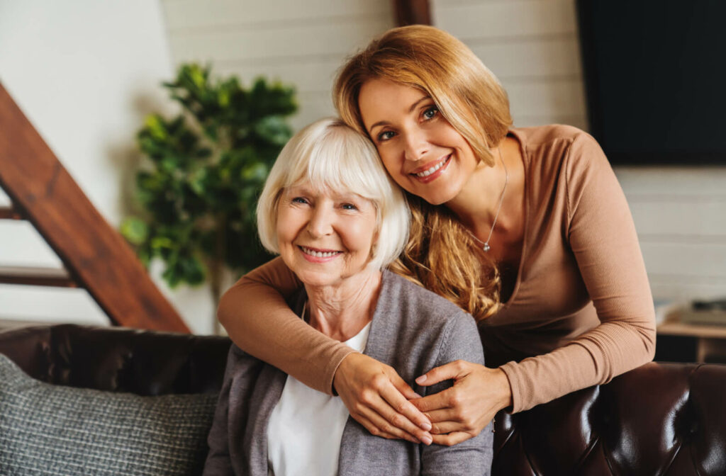 An adult hugging their older parent from behind while visiting them in assisted living.